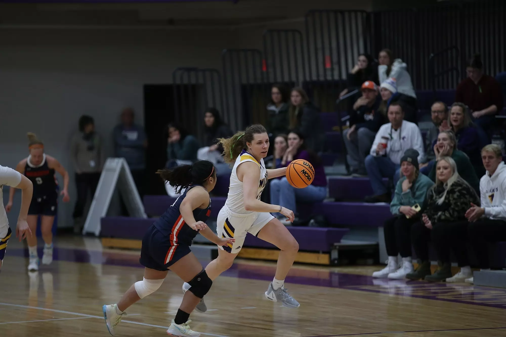 St. Catherine player dribbling down the court as Macalster player guards